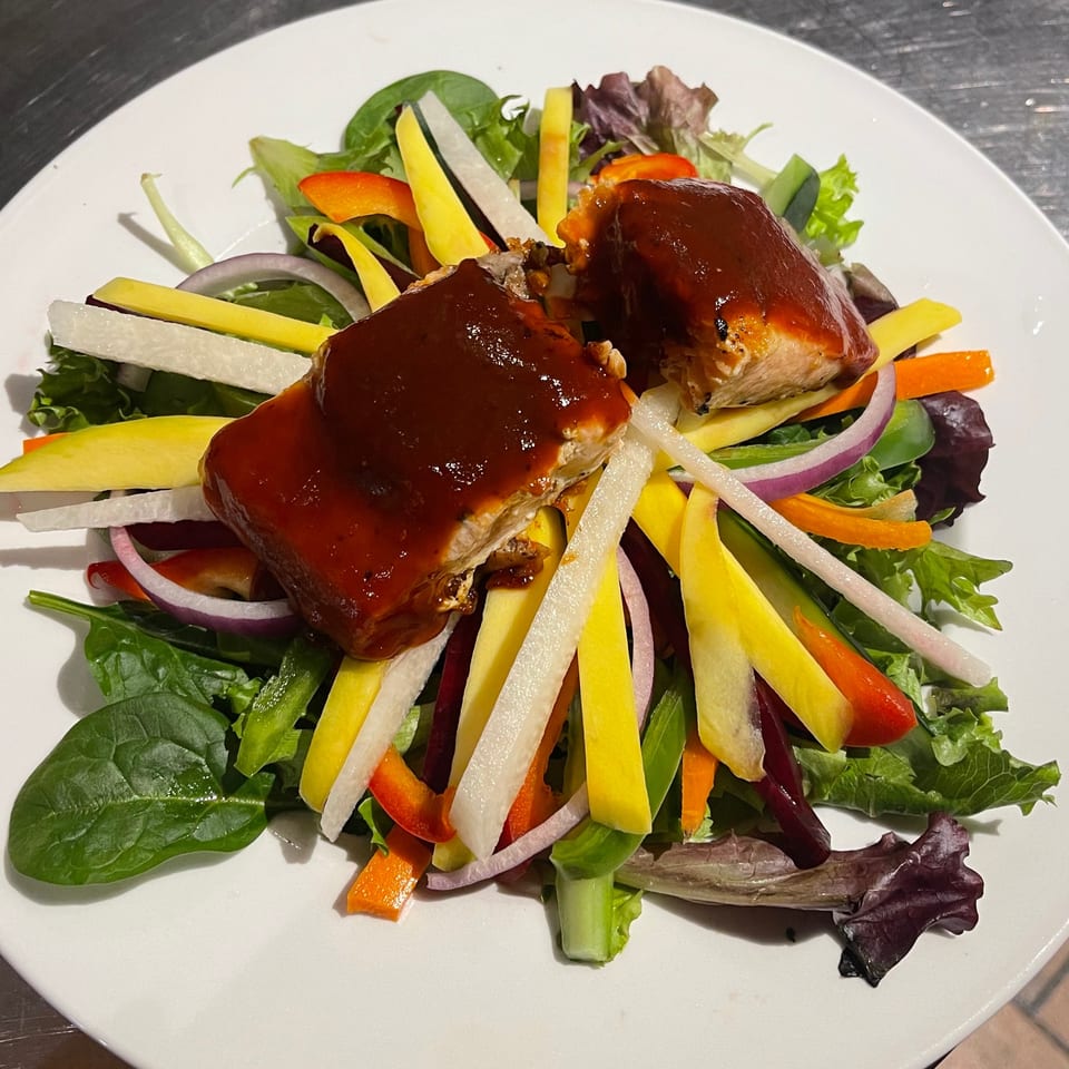 Two pieces of salmon with dark sauce on a colorful salad with mango, radish, and bell peppers.