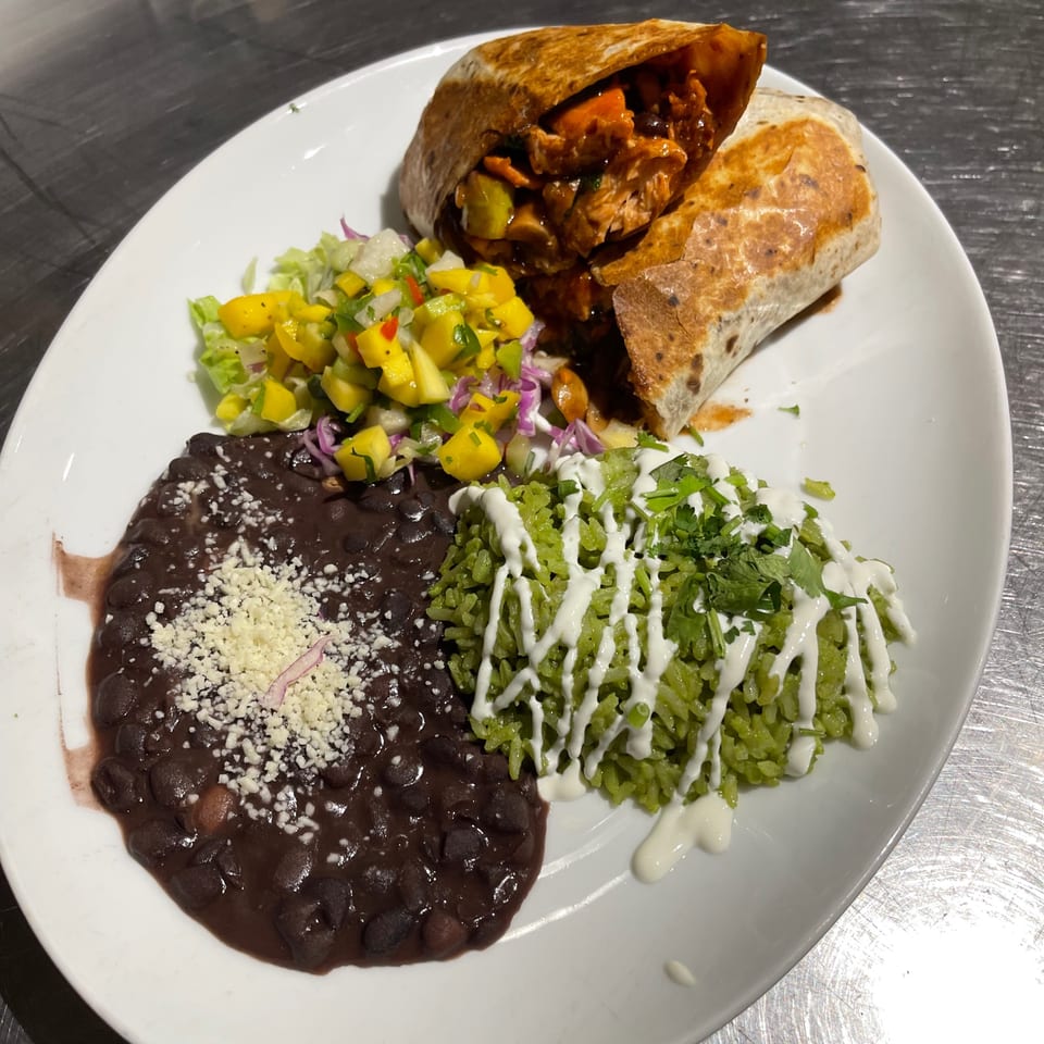 A chicken burrito with mango salsa, black beans, and green rice on a white plate.