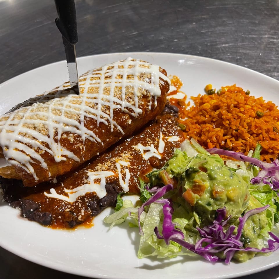 Two enchiladas with red sauce, sour cream, rice, black beans, and a side salad with guacamole.
