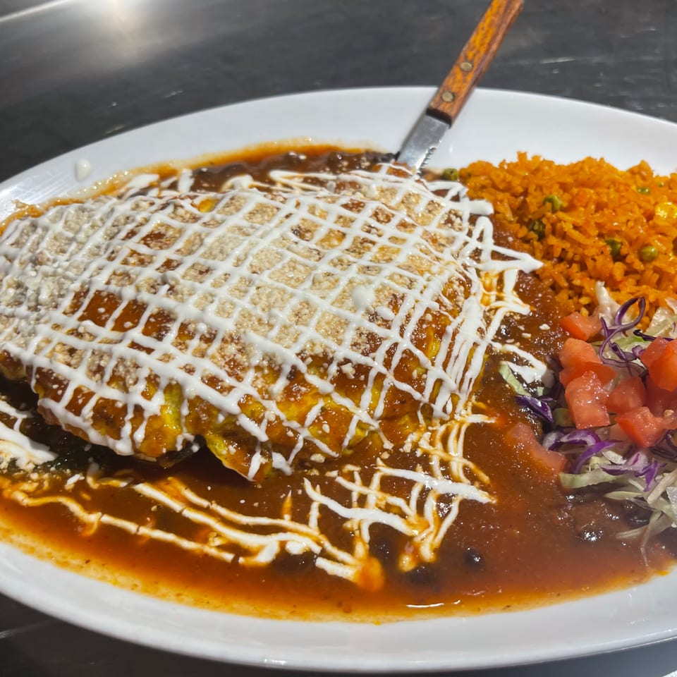 A large plate of Mexican food with a knife, featuring a main dish drizzled with white sauce, rice, and salad.